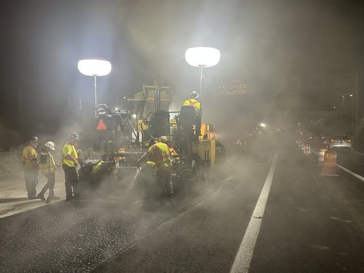Steam from newly laid pavement rises around Wright Brothers' crews,